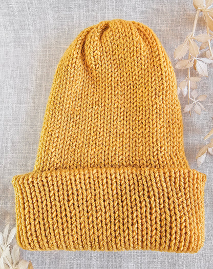 Knitted mustard yellow beanie on a textured light gray background