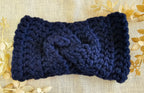 Navy blue knitted headband on a textured beige background with gold leaves.