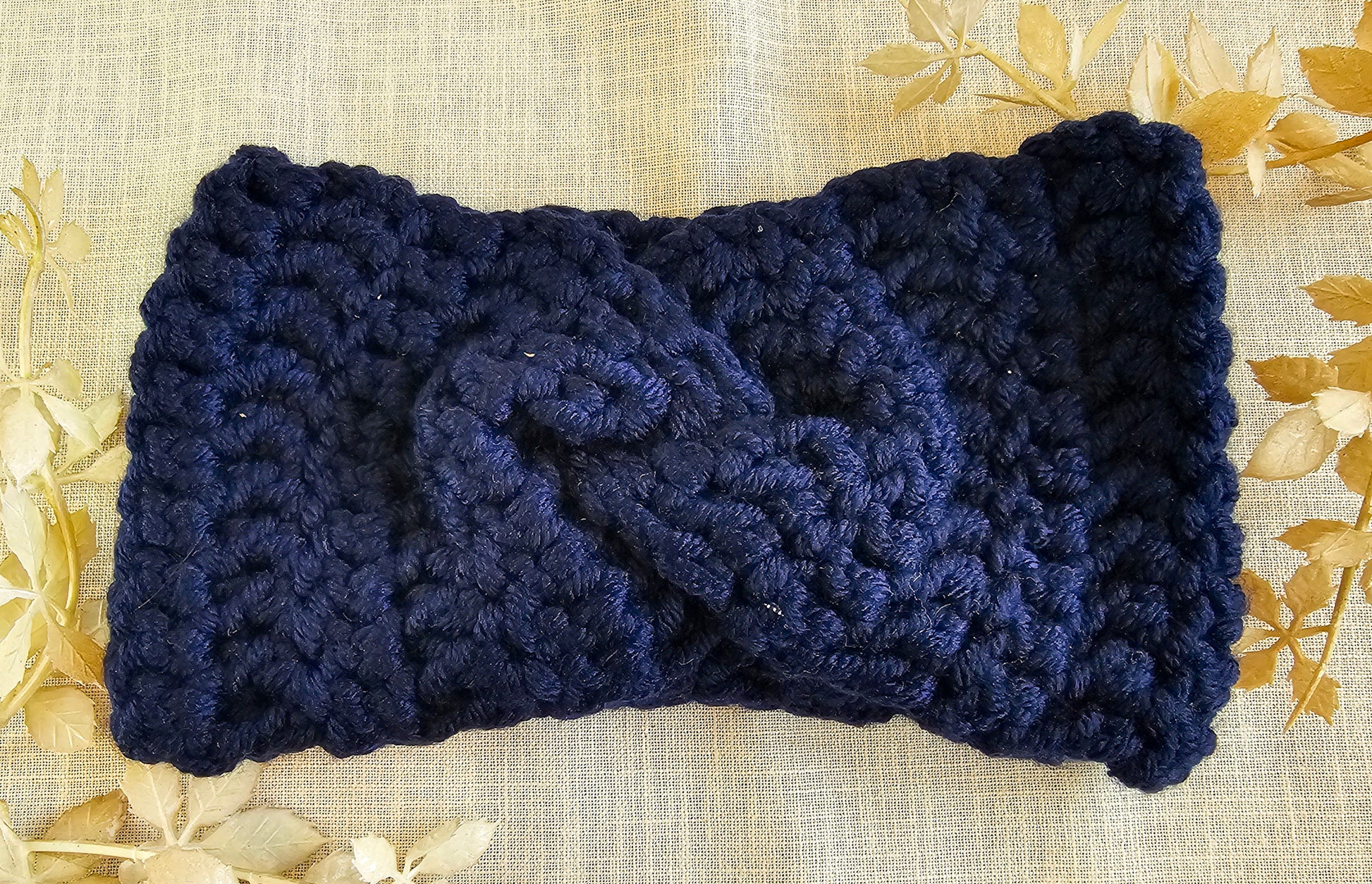 Navy blue knitted headband on a textured beige background with gold leaves.