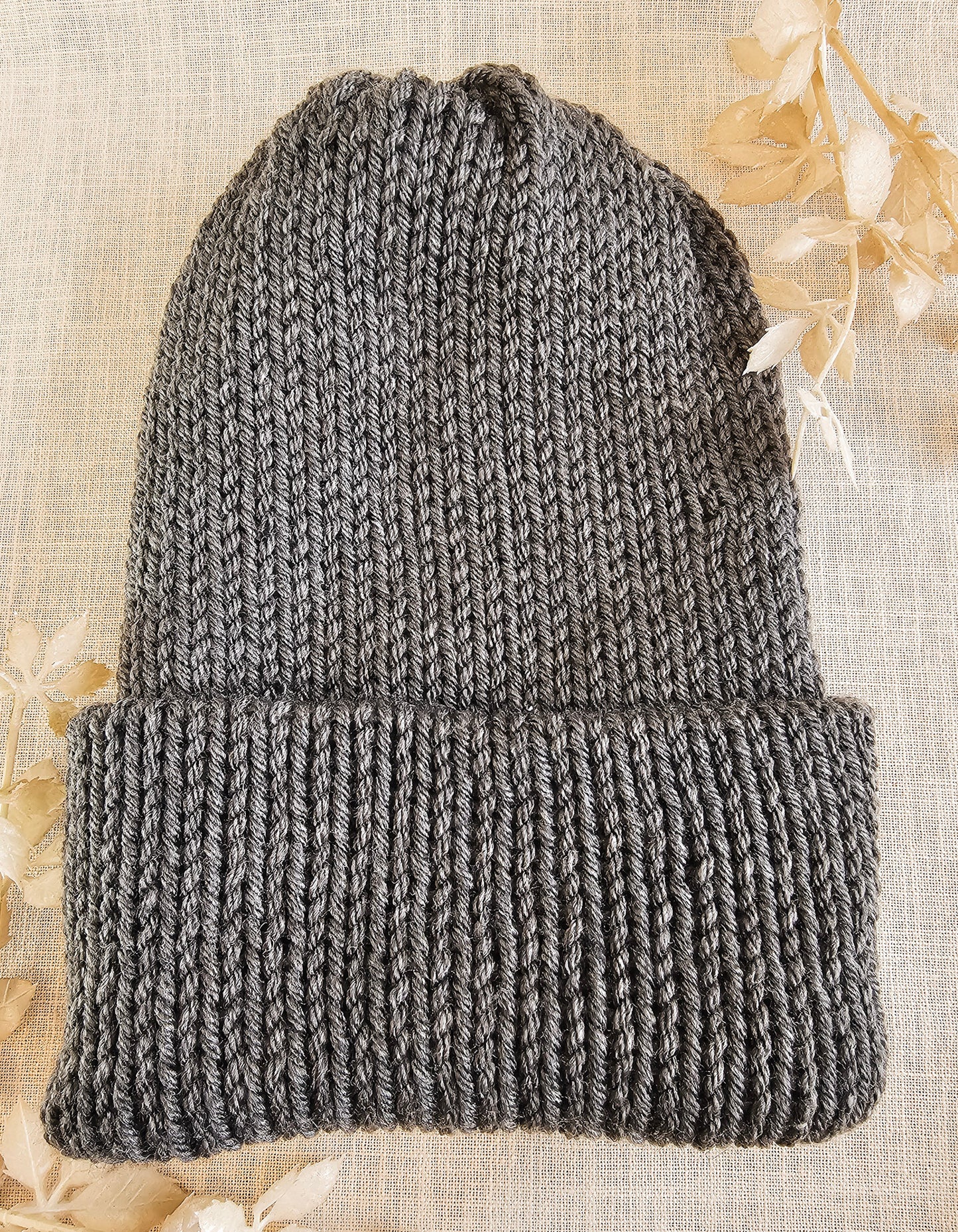 Gray knitted beanie on a textured beige background with dried flowers.