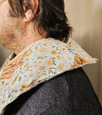 A close-up side view of a person wearing  hot and cold neck packgreen, and brown tones on an off-white background, paired with a dark gray textured jacket.