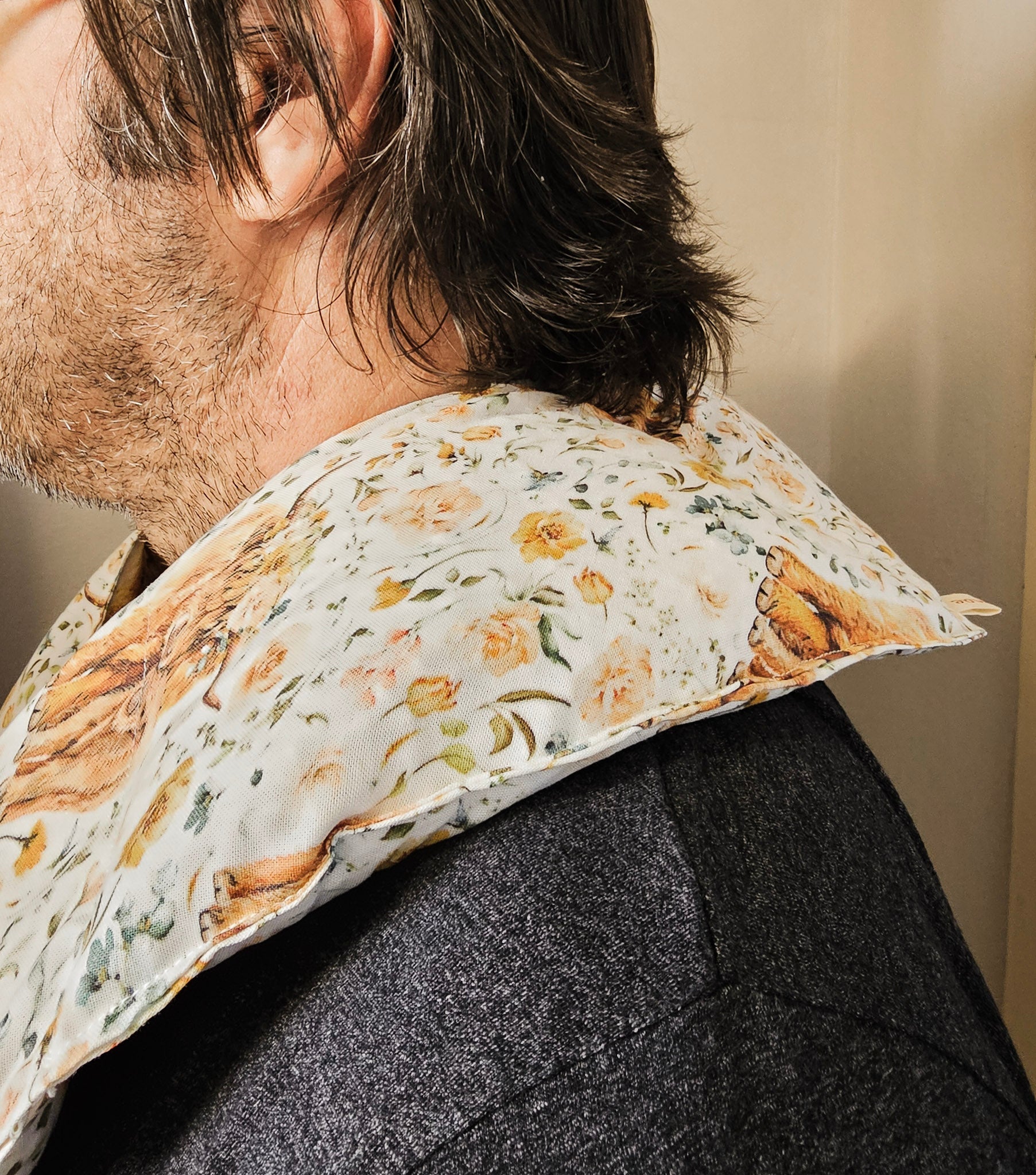 A close-up side view of a person wearing  hot and cold neck packgreen, and brown tones on an off-white background, paired with a dark gray textured jacket.