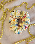Koala Clause pale yellow Christmas scrunchie with koalas in Santa hats and colourful surfboards, laid flat beside gold beads.