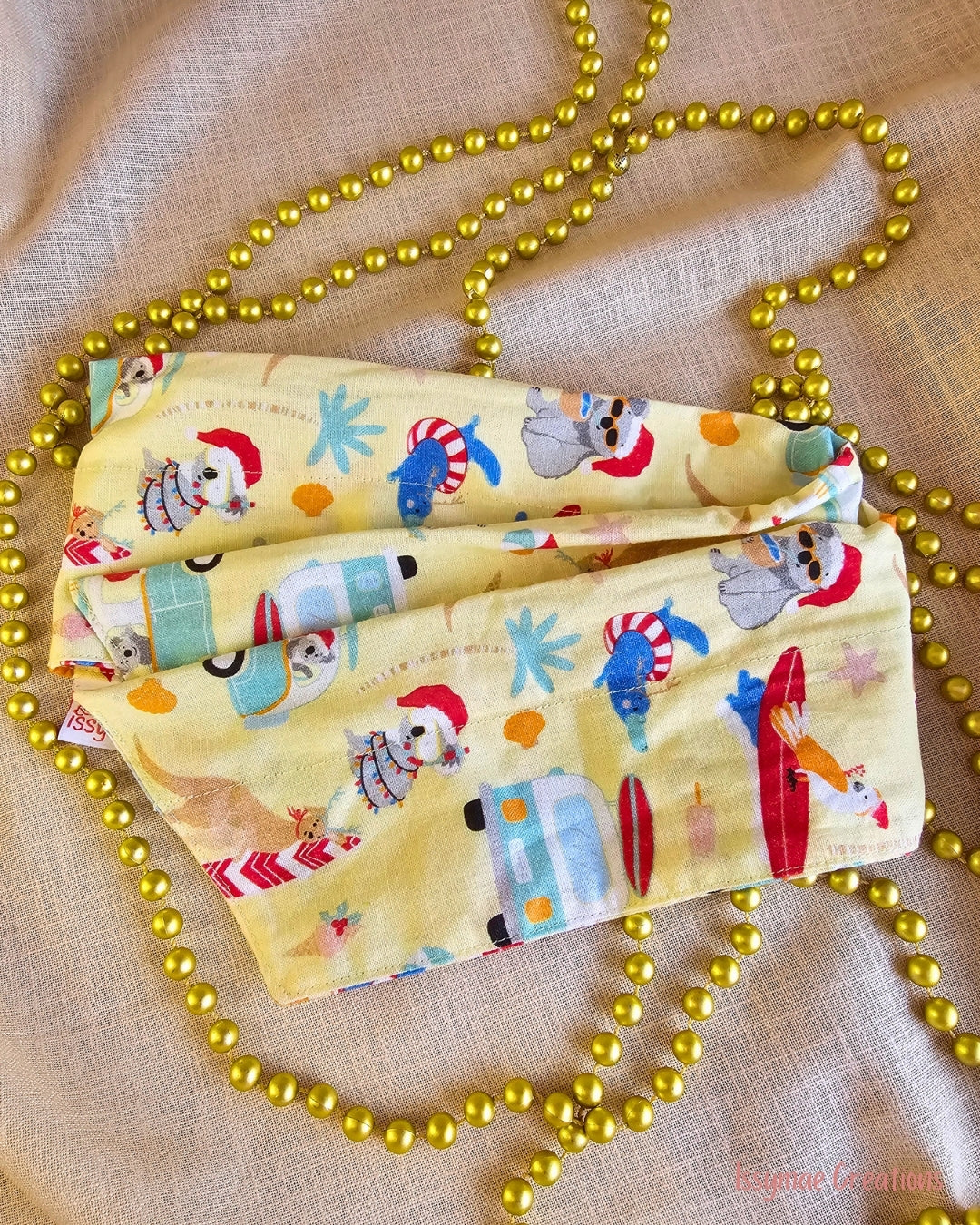 Koala Clause wire head wrap laid flat, featuring Christmas koalas, surfboards and campervans on pale yellow fabric.