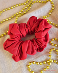 Santa Baby handmade red Christmas scrunchie laid flat on cream fabric, surrounded by gold Christmas beads.