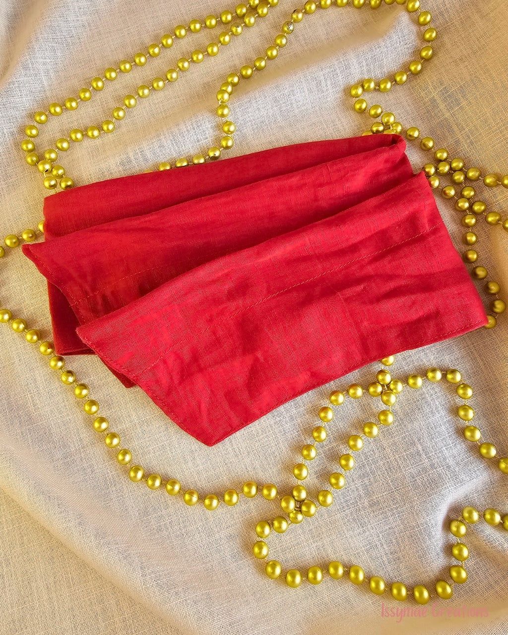 Santa Baby red wire head wrap laid flat on cream fabric with gold Christmas beads.