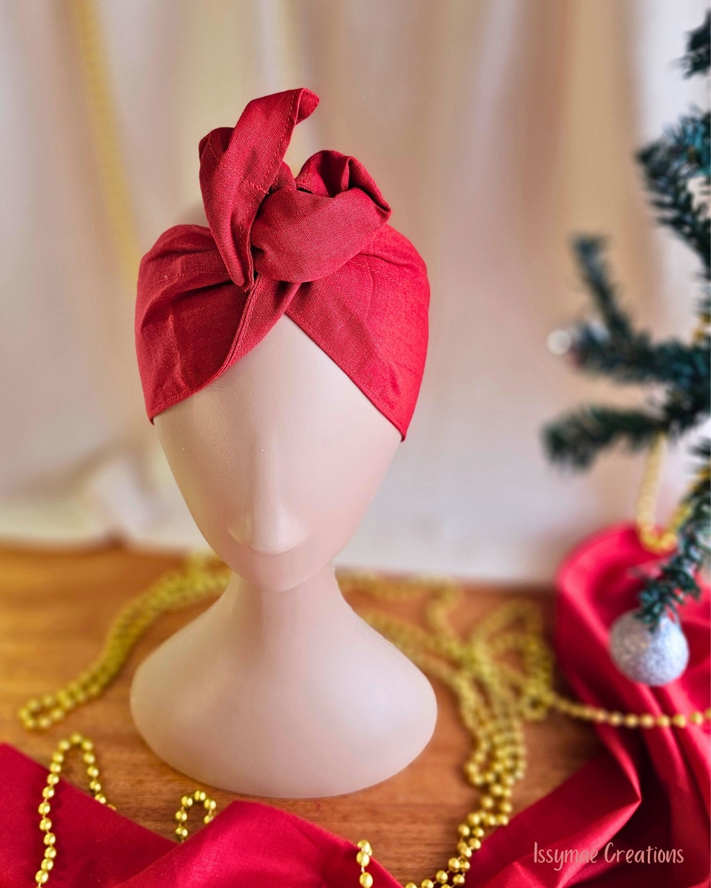 Red wire head wrap with a sculpted top knot, displayed on a mannequin beside Christmas decorations.