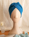 Front view of mannequin wearing a teal knotted headband with cream linen background