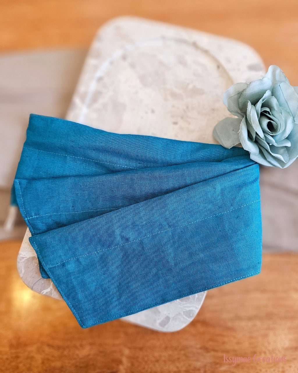 Flat view of teal wire head band with blue flower and stone plate