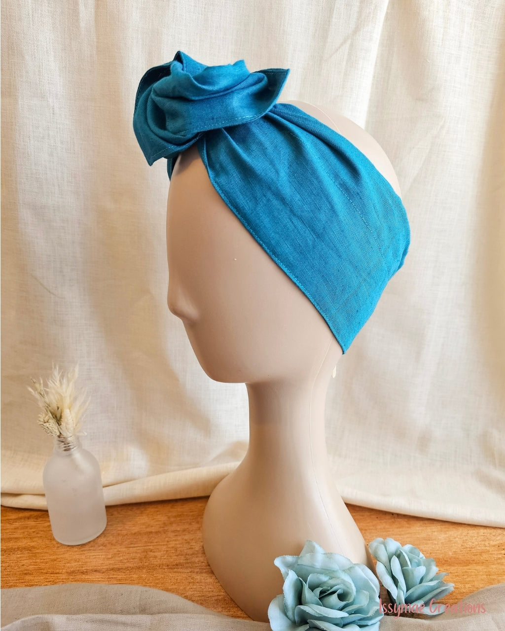 Teal womans wire headwrap side view on mannequin head with jar flowers and liene background