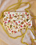 Vintage Greetings wire head wrap laid flat, showing poinsettias, baubles and Christmas illustrations on cream fabric.