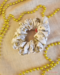 Frosted Holly white Christmas scrunchie with gold and silver holly print, laid flat on cream fabric beside gold beads.