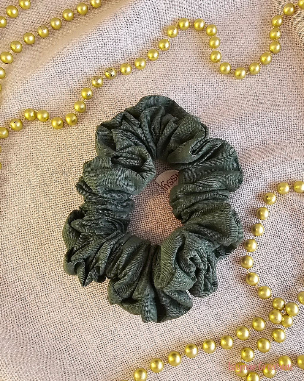 Evergreen Envy dark green Christmas scrunchie laid flat on cream fabric, surrounded by gold Christmas beads.