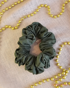 Evergreen Envy dark green Christmas scrunchie laid flat on cream fabric, surrounded by gold Christmas beads.