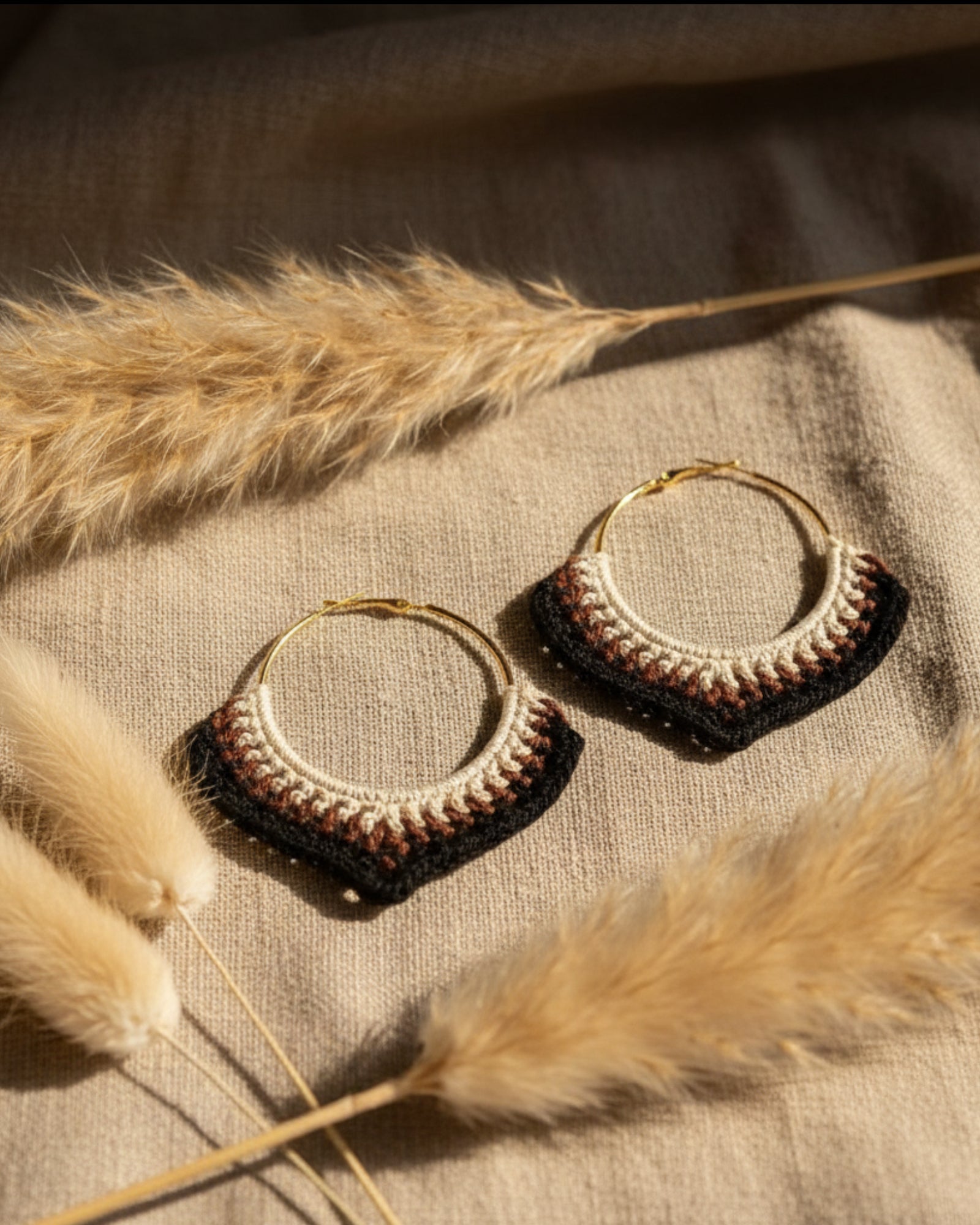 Gold hoop earrings with intricate detailing on a textured surface with dried grasses.