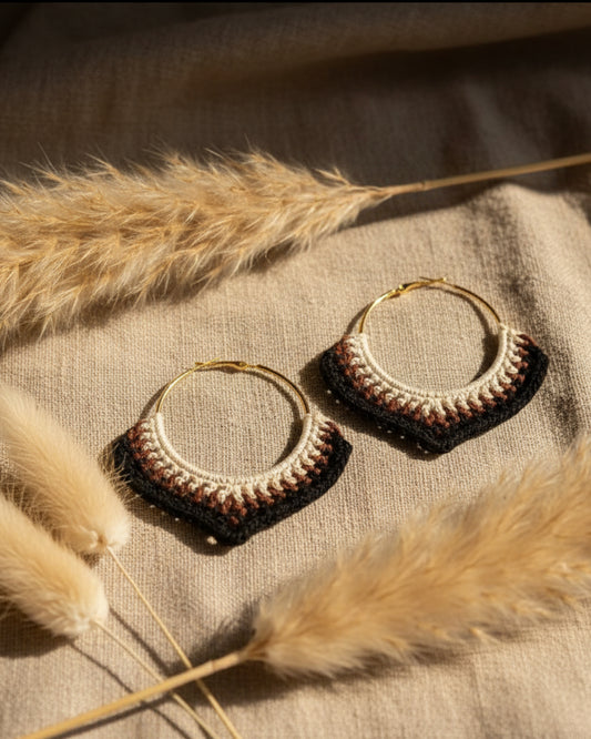 Gold hoop earrings with intricate detailing on a textured surface with dried grasses.