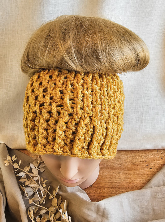 Person wearing a mustard yellow knitted headband with a neutral background