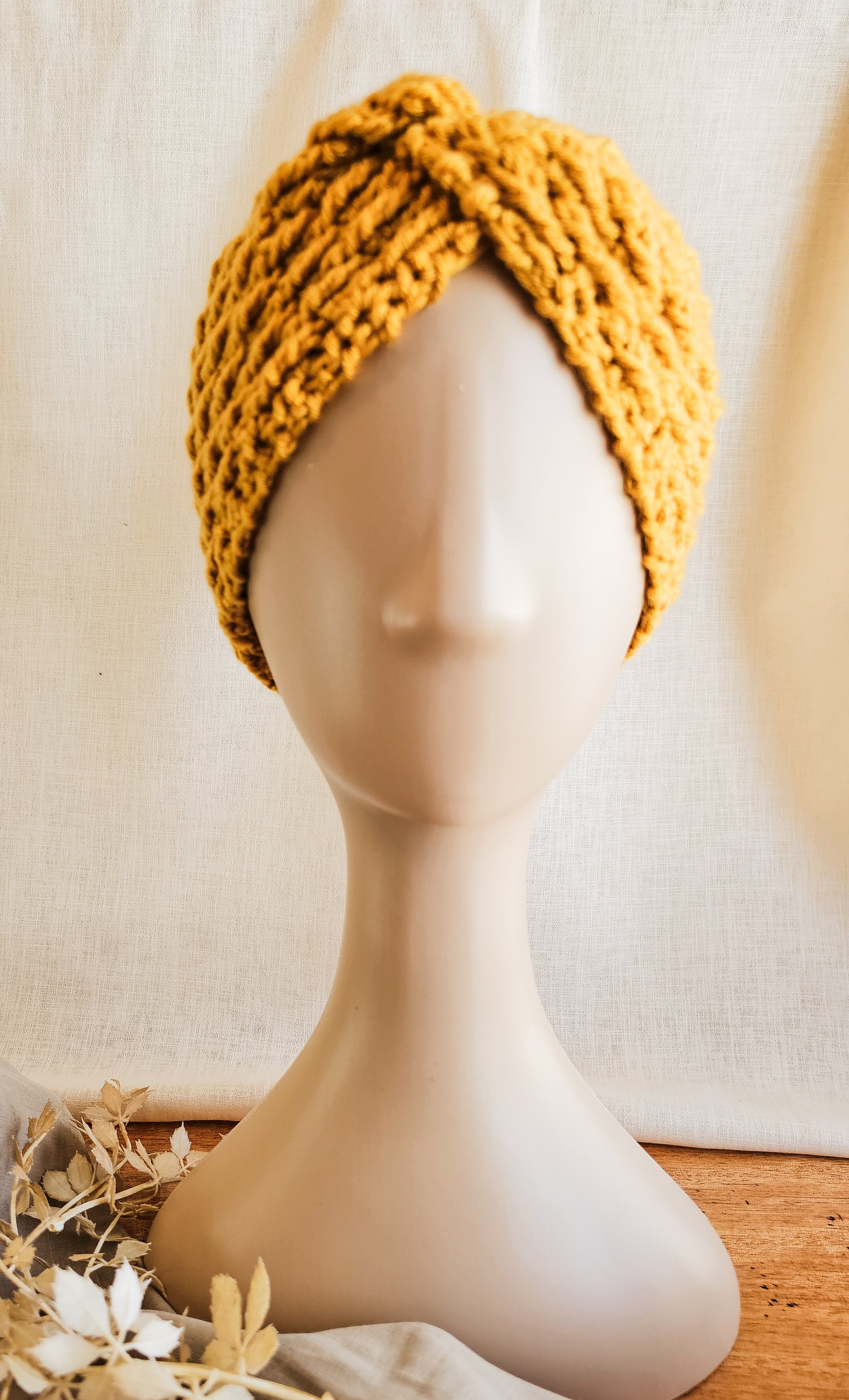 Yellow knitted turban on a mannequin head against a neutral background
