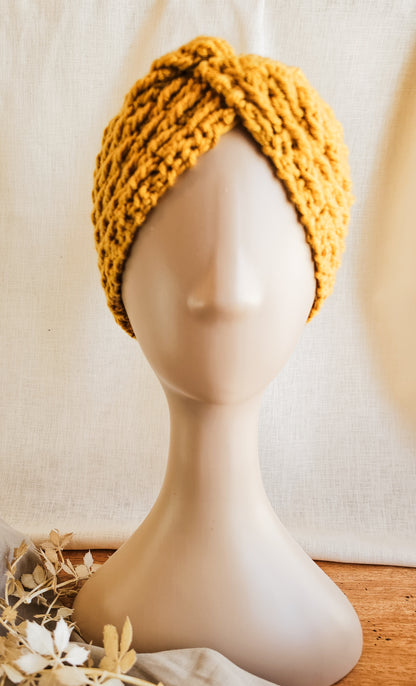 Yellow knitted turban on a mannequin head against a neutral background
