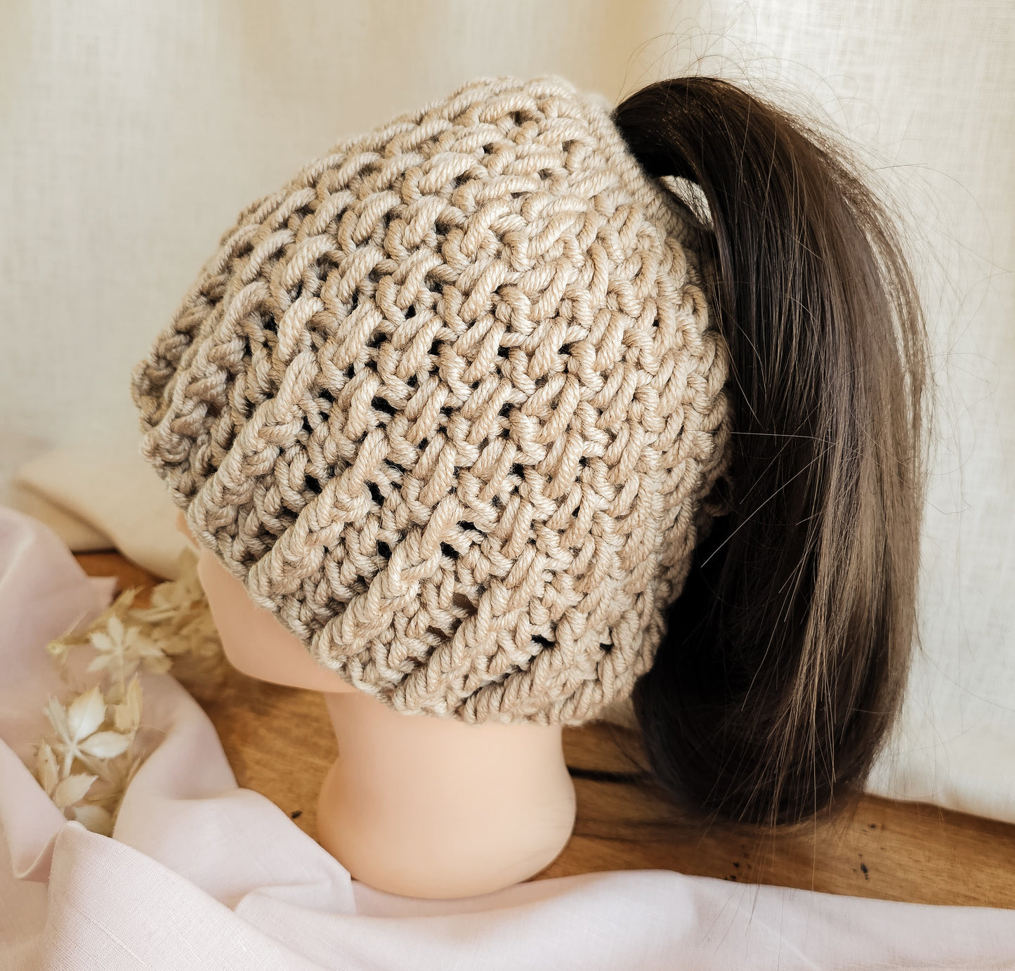 Beige knitted headband worn by a mannequin head with a blurred background