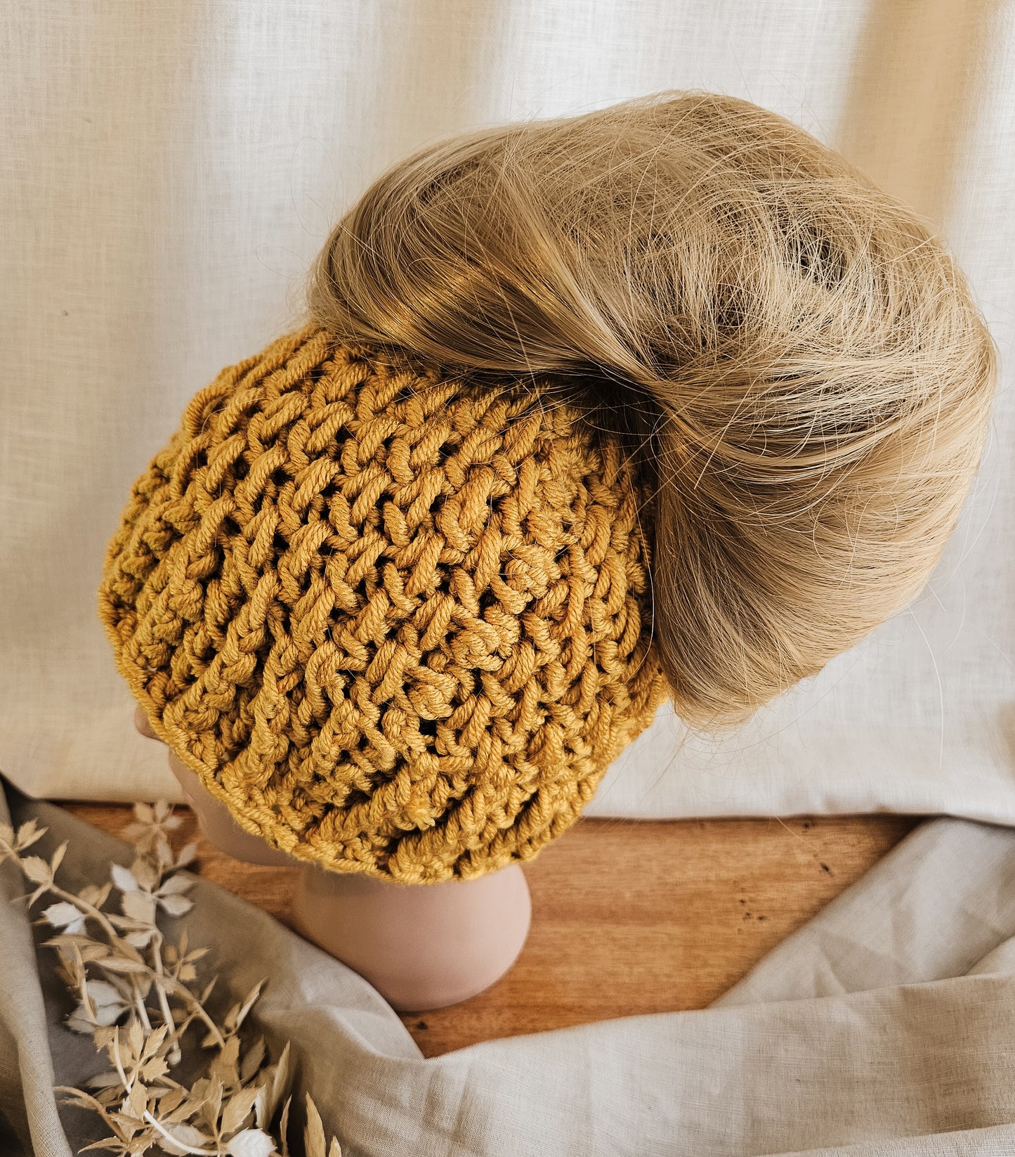 Person wearing a mustard yellow knitted headband with a neutral background
