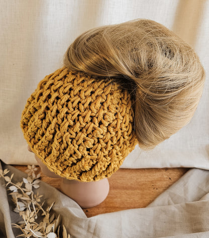 Person wearing a mustard yellow knitted headband with a neutral background