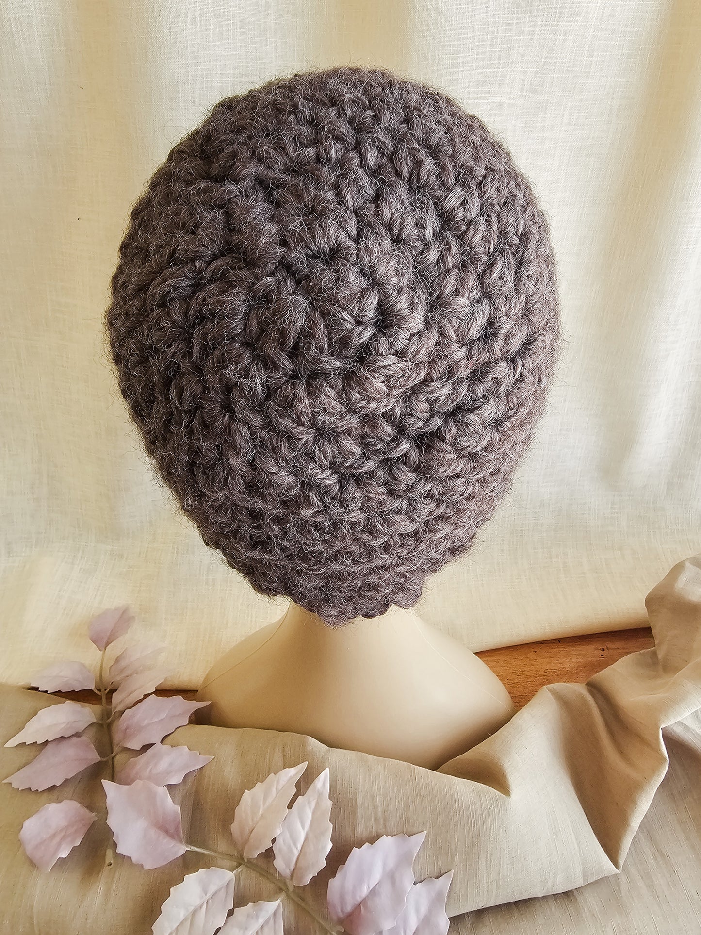 Crocheted brown hat on a mannequin head with a soft beige background