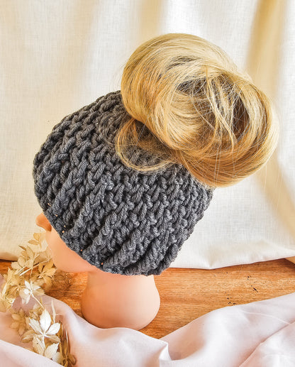 Gray knitted bun hat worn by a person with a bun, on a neutral background.