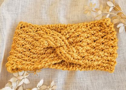 Mustard yellow knitted headband on a textured beige background with floral elements.