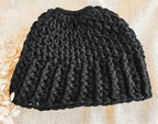 Black knitted beanie on a textured beige surface