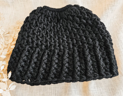 Black knitted beanie on a textured beige surface
