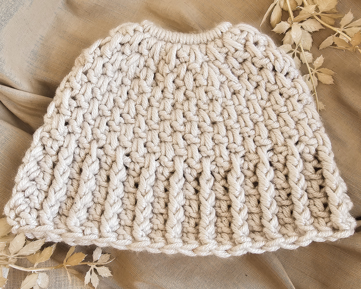 Beige knitted hat on a beige fabric background with floral decorations