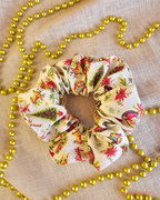Vintage Greetings cream Christmas scrunchie wth retro reindeer, poinsettias and Christmas trees, laid flat beside gold beads.